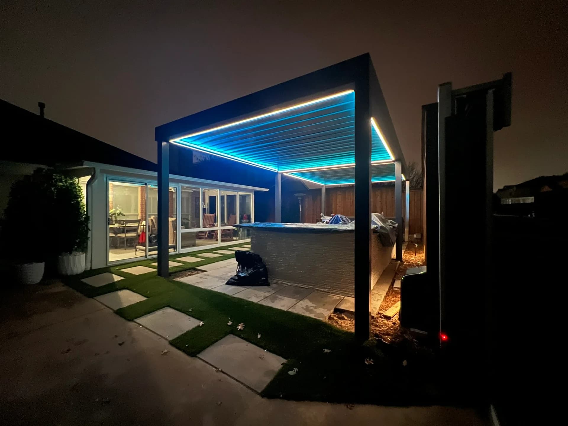 Dark aluminum louvered pergola with LED-lit beams over a stone patio at night