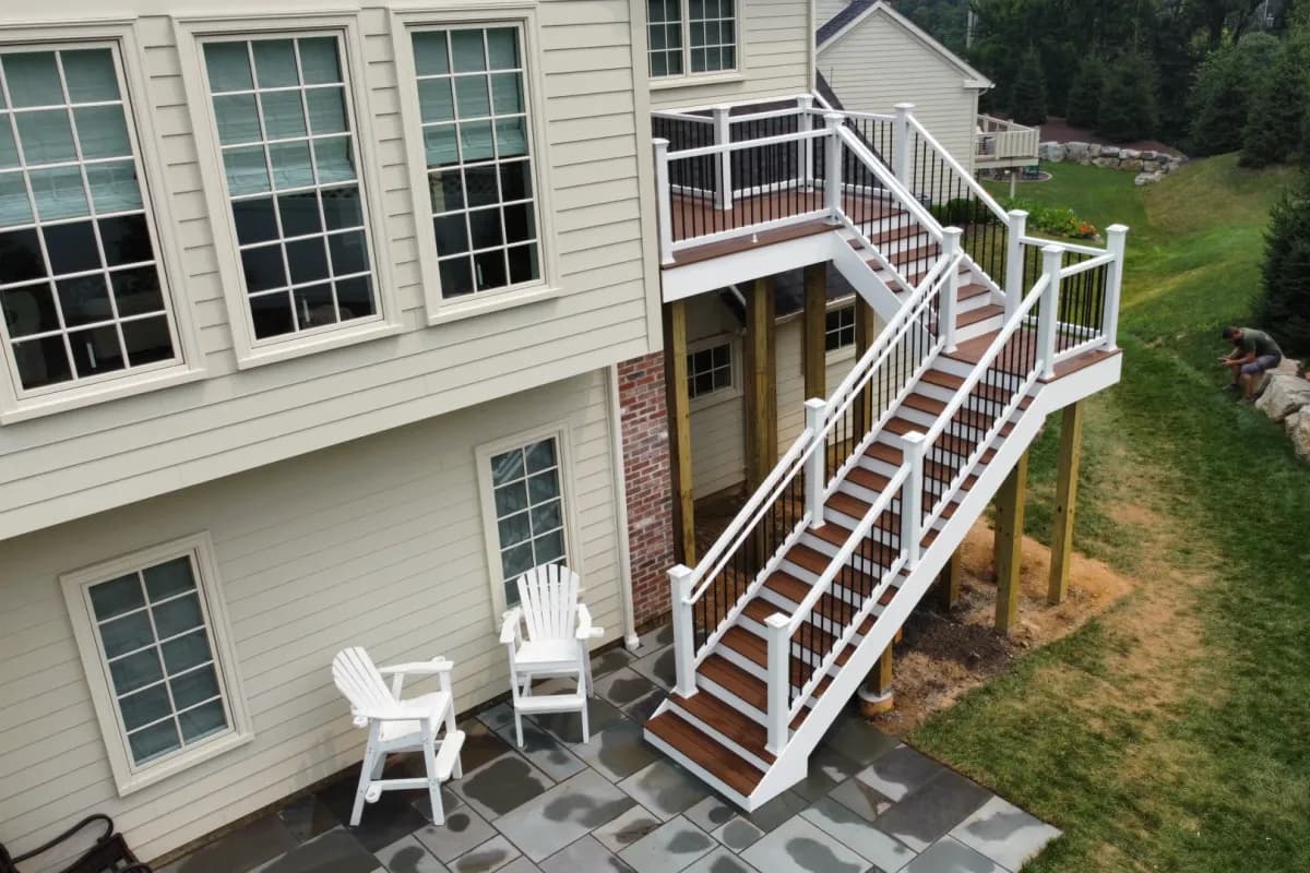 Gray stone patio at the foot of a white-railed elevated deck stair