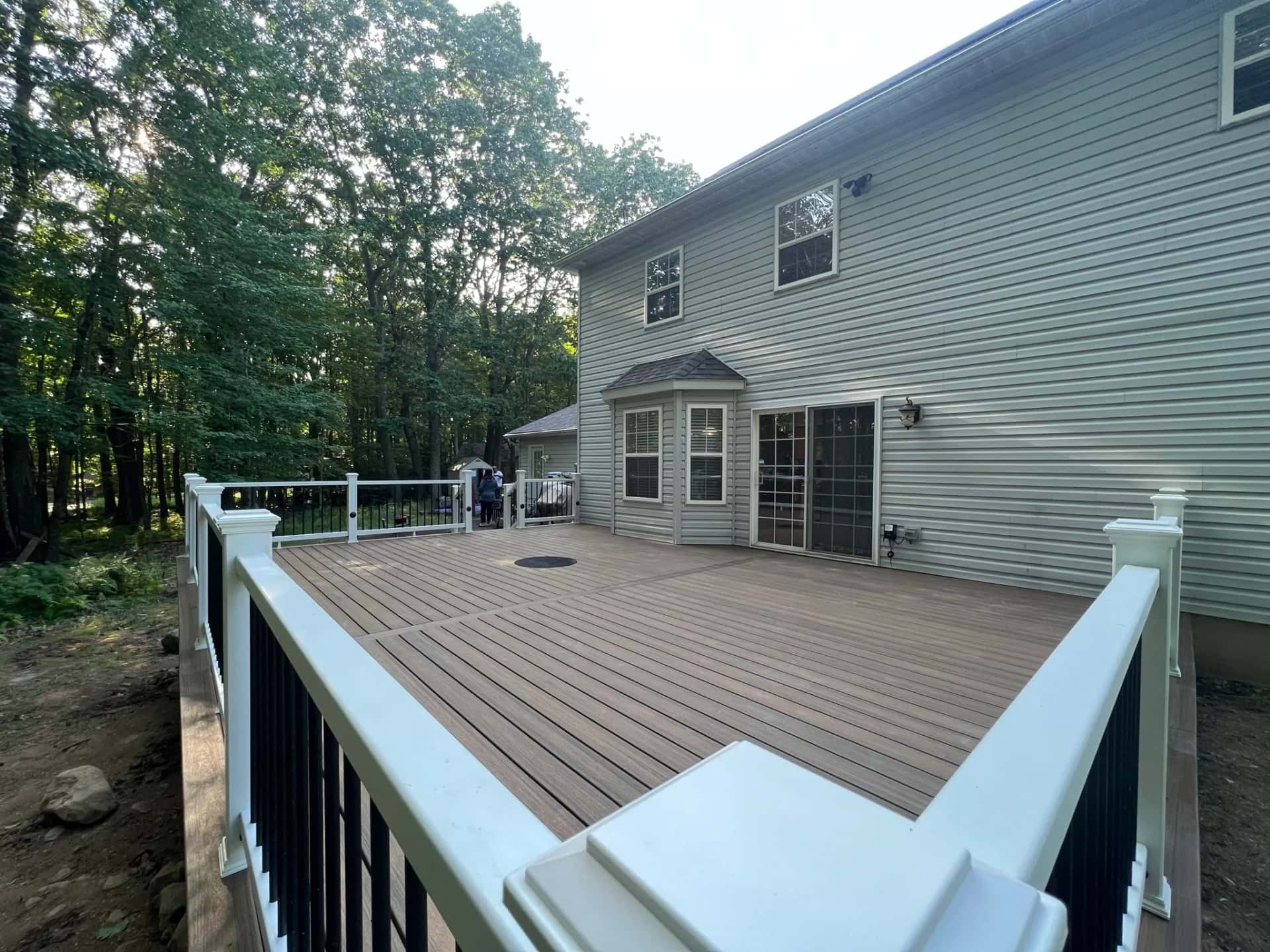 Composite deck with white railing and black balusters against a wooded backyard