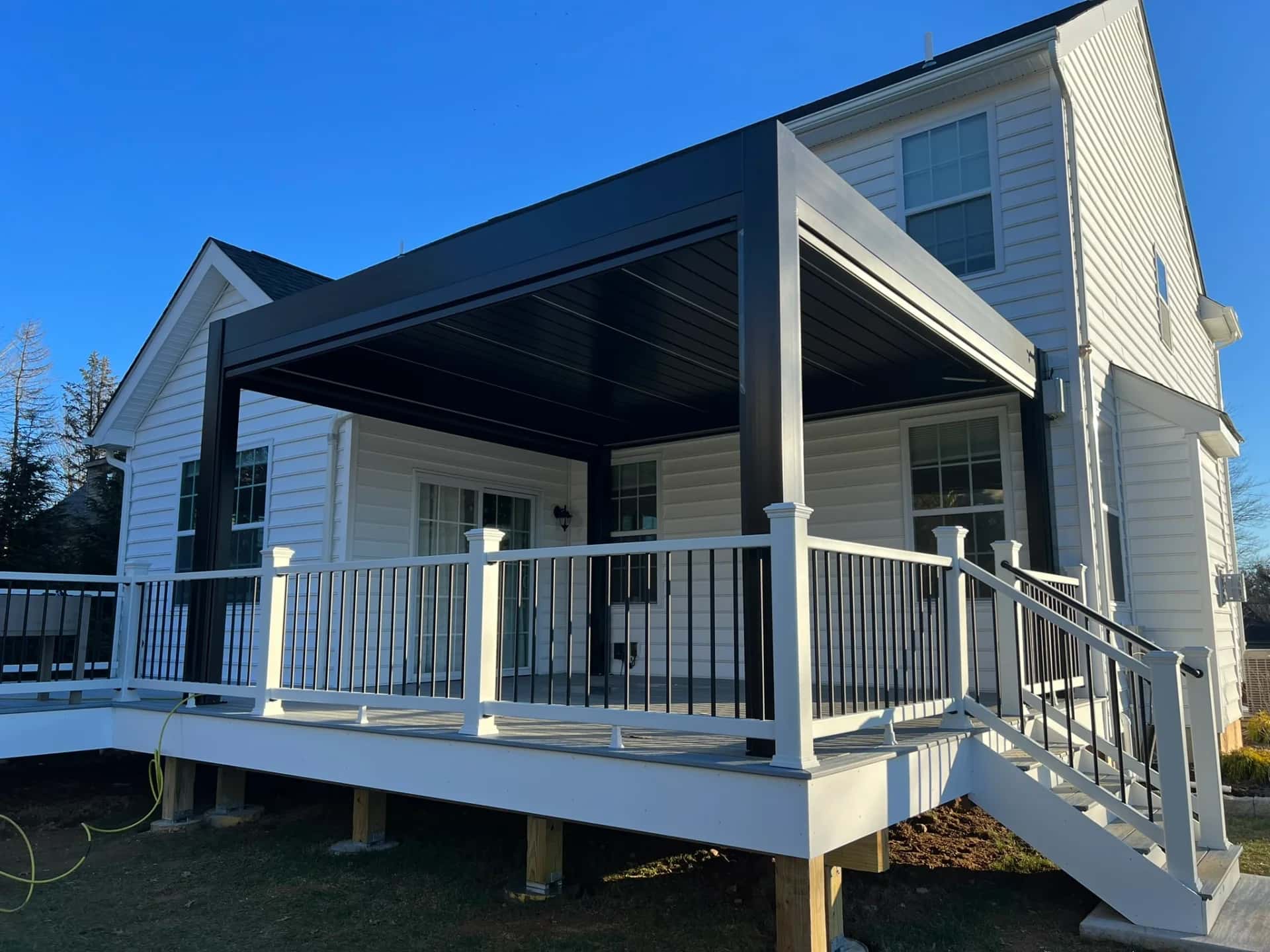 Covered composite deck with a black louvered pergola, white railing, black balusters and stairs