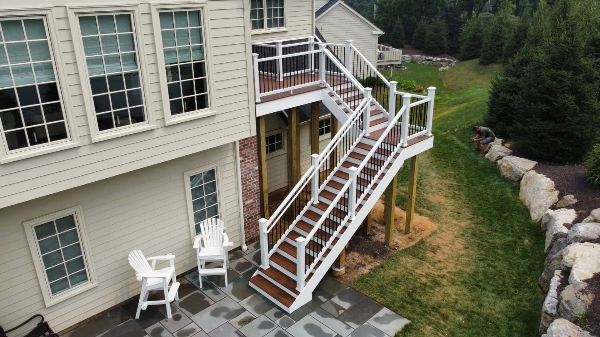 Elevated brown composite deck with white railing and stairs down to a bluestone paver patio