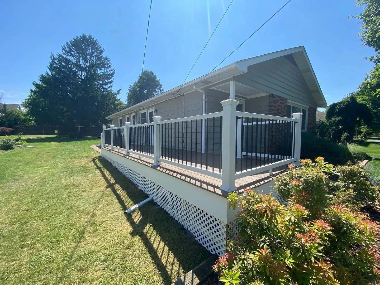 Long composite deck with white vinyl railing, black balusters, lattice skirting and landscaping
